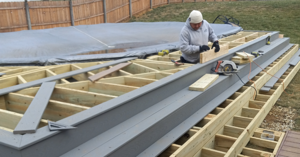 Image showing "Worker installing gray deck boards on a wooden frame.